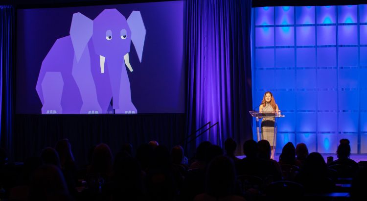 Corina Tracy on stage with elephant on screen